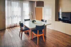 Ein moderner Essbereich mit einem Glastisch, Holzsesseln, einem Kübelorchidee und einem Fernseher an der Wand.
