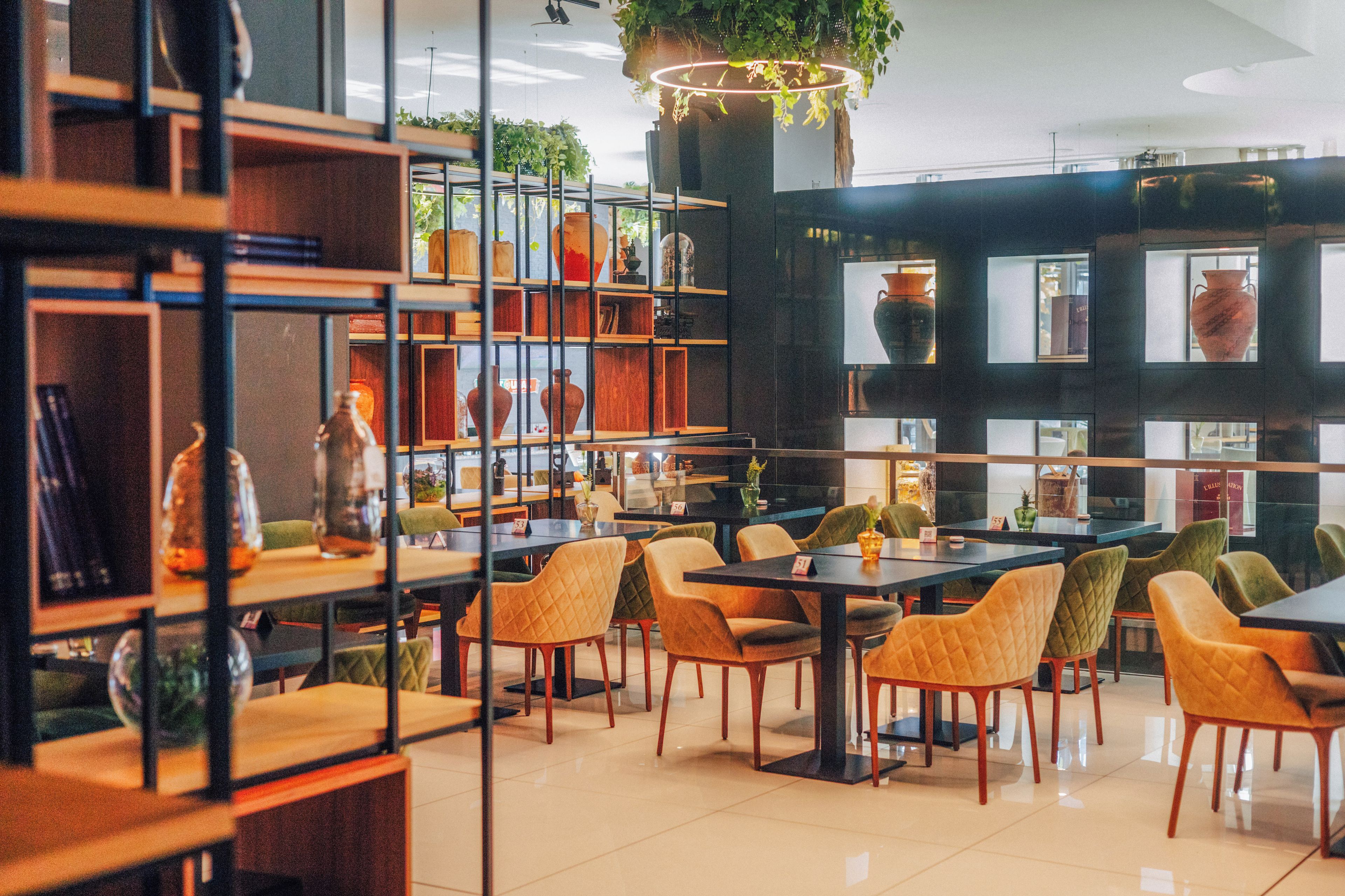 A restaurant with a modern interior, featuring wooden tables and chairs, and shelves with various items.