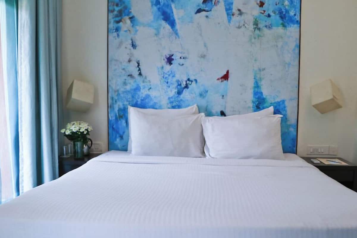 Habitación de hotel con una cama grande, ropa de cama blanca, un cuadro abstracto azul en la pared y dos lámparas de noche.