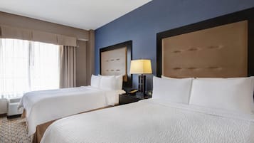 Una habitación de hotel con dos camas, una mesita de noche con lámpara y un ventanal con cortinas.