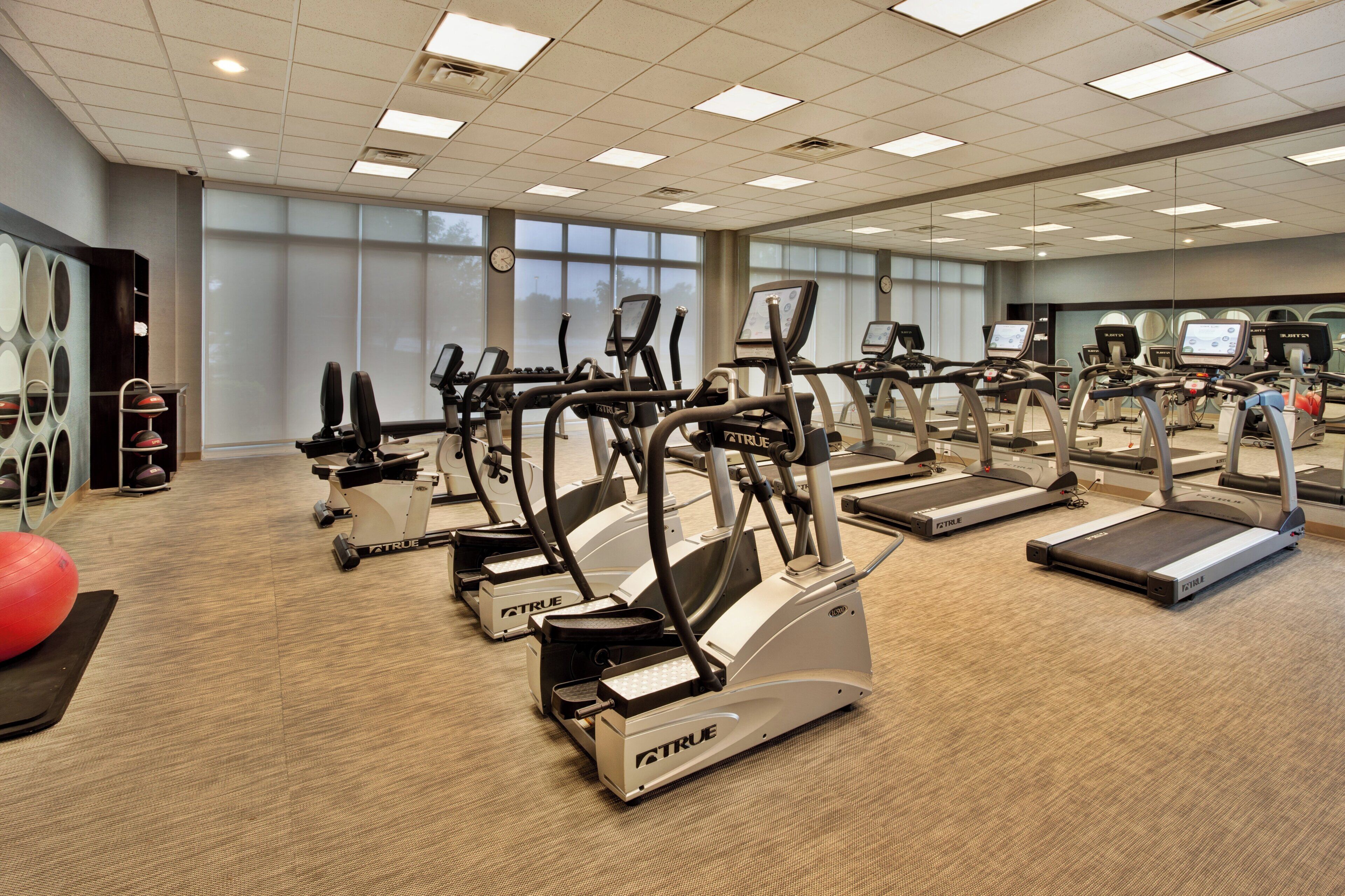 A gym with multiple exercise machines, including treadmills and elliptical trainers, arranged in rows.