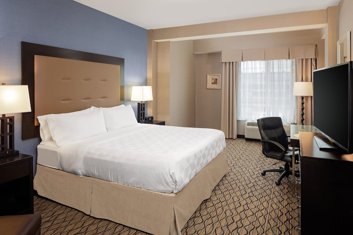 A hotel room with a large bed, a desk with a computer, a TV, and two lamps.