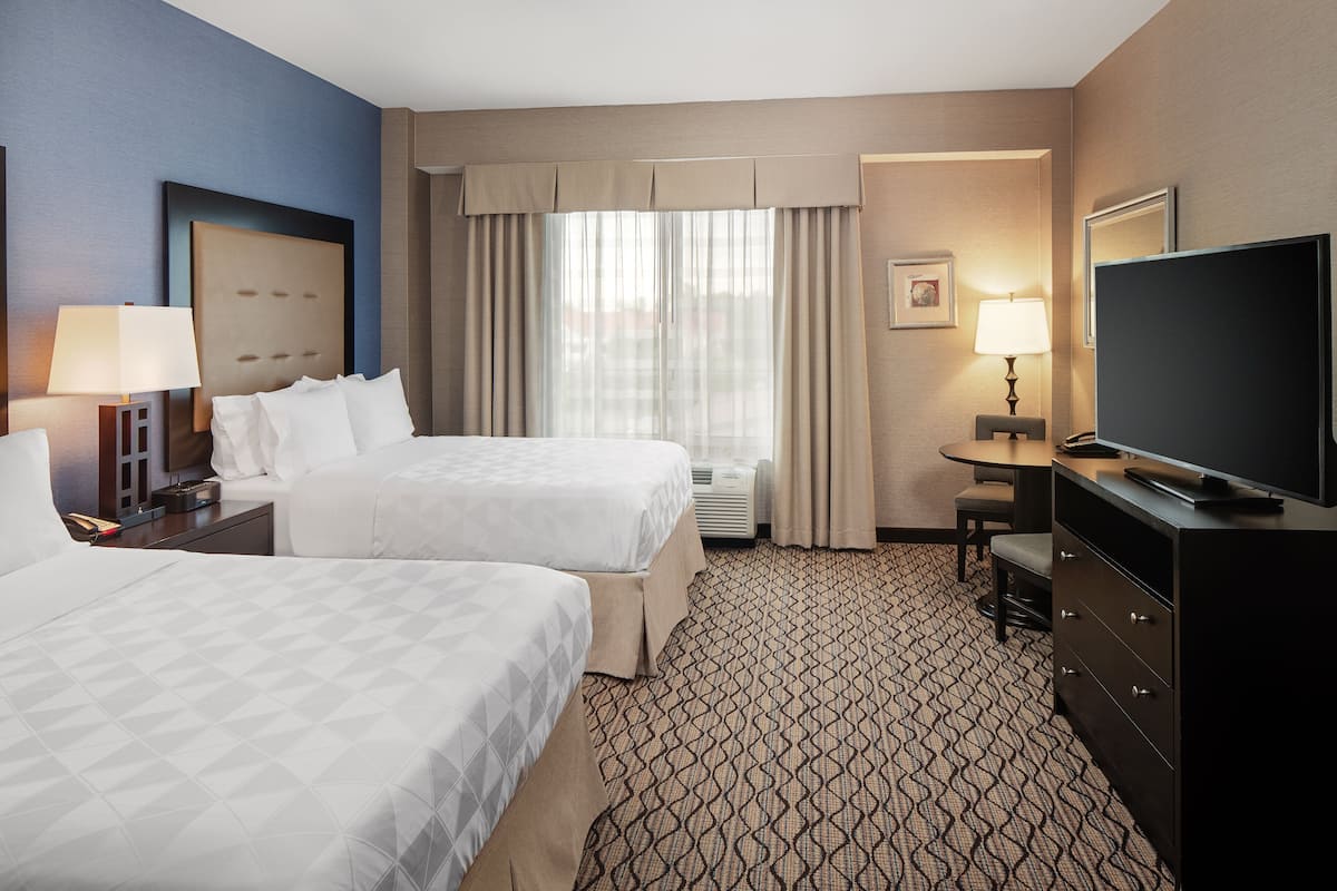 A hotel room with two beds, a television, a desk, and a chair.
