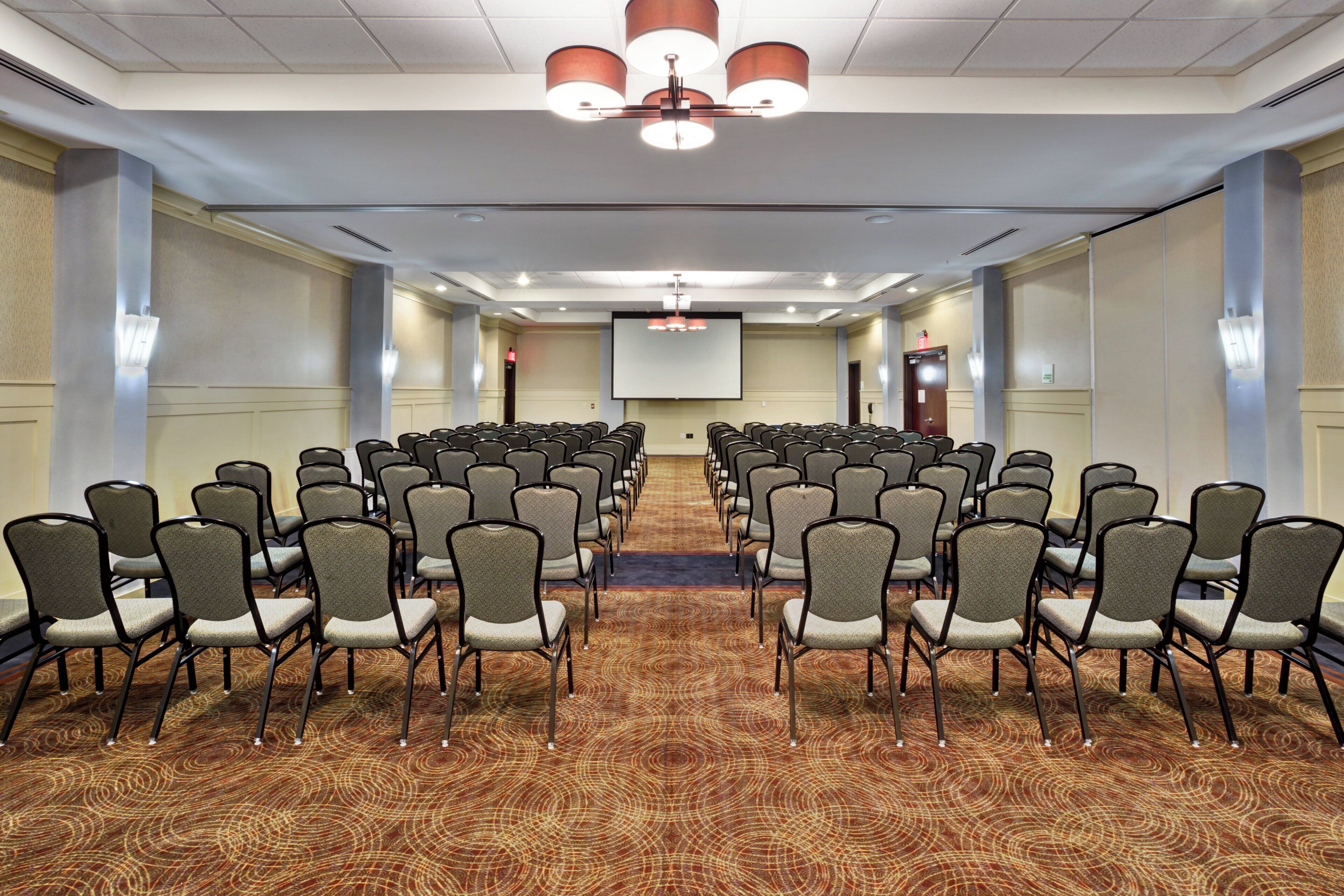 A conference room with rows of chairs, a projector screen, and a carpeted floor.