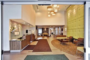 A hotel lobby with a reception desk, seating area, and a fireplace. - Holiday Inn Detroit Metro Airport by IHG (Romulus)