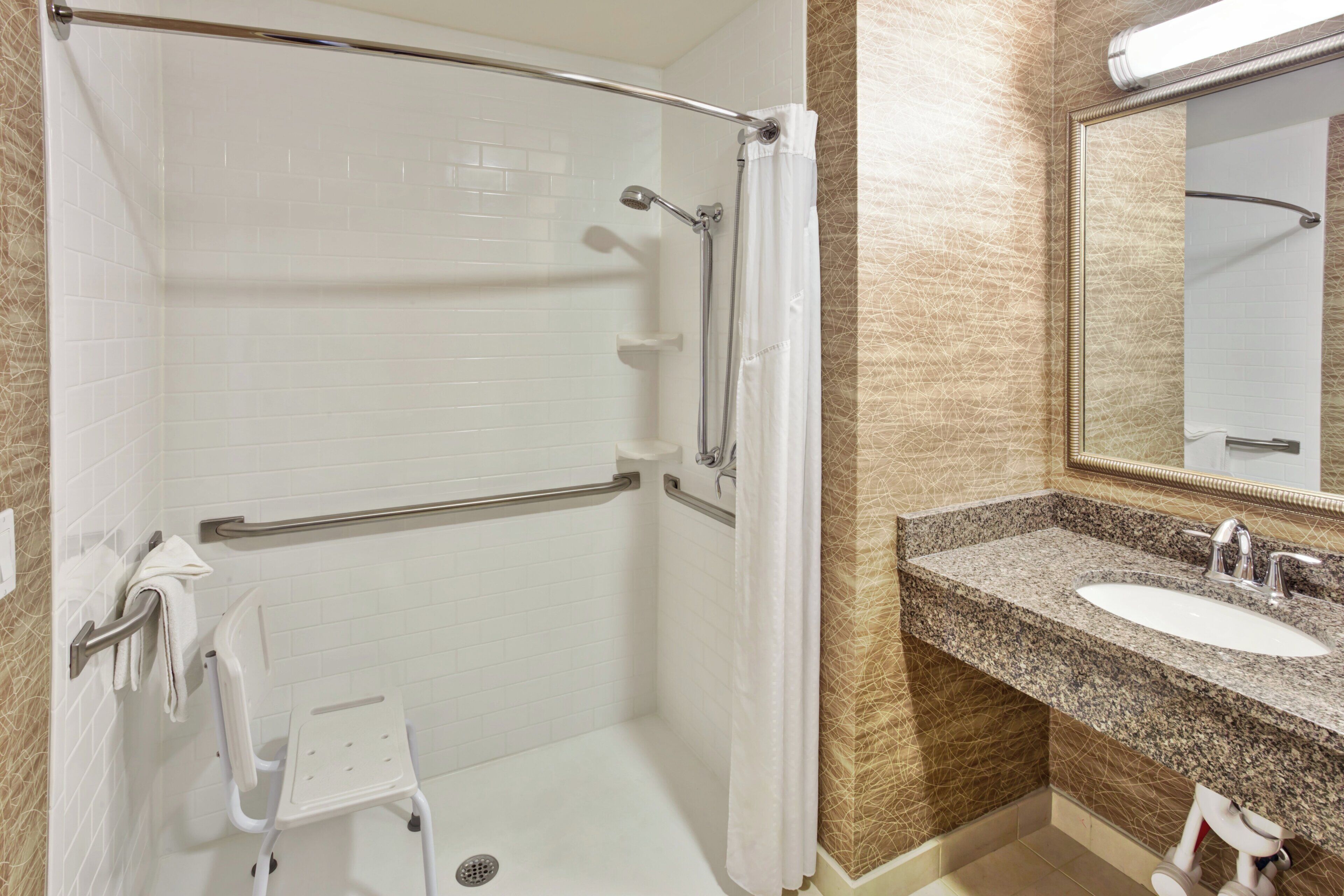 A bathroom with a shower, grab bars, a sink, and a mirror.