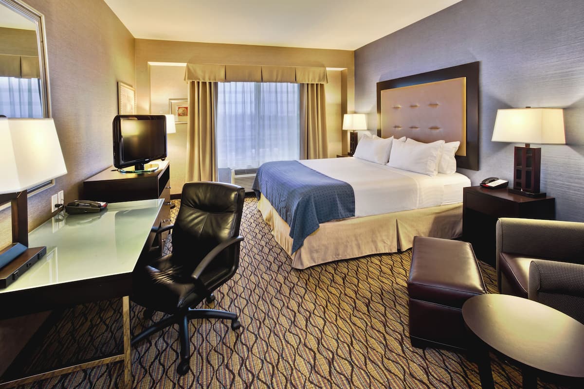 A hotel room with a bed, a desk with a computer, a chair, a TV, and a lamp.
