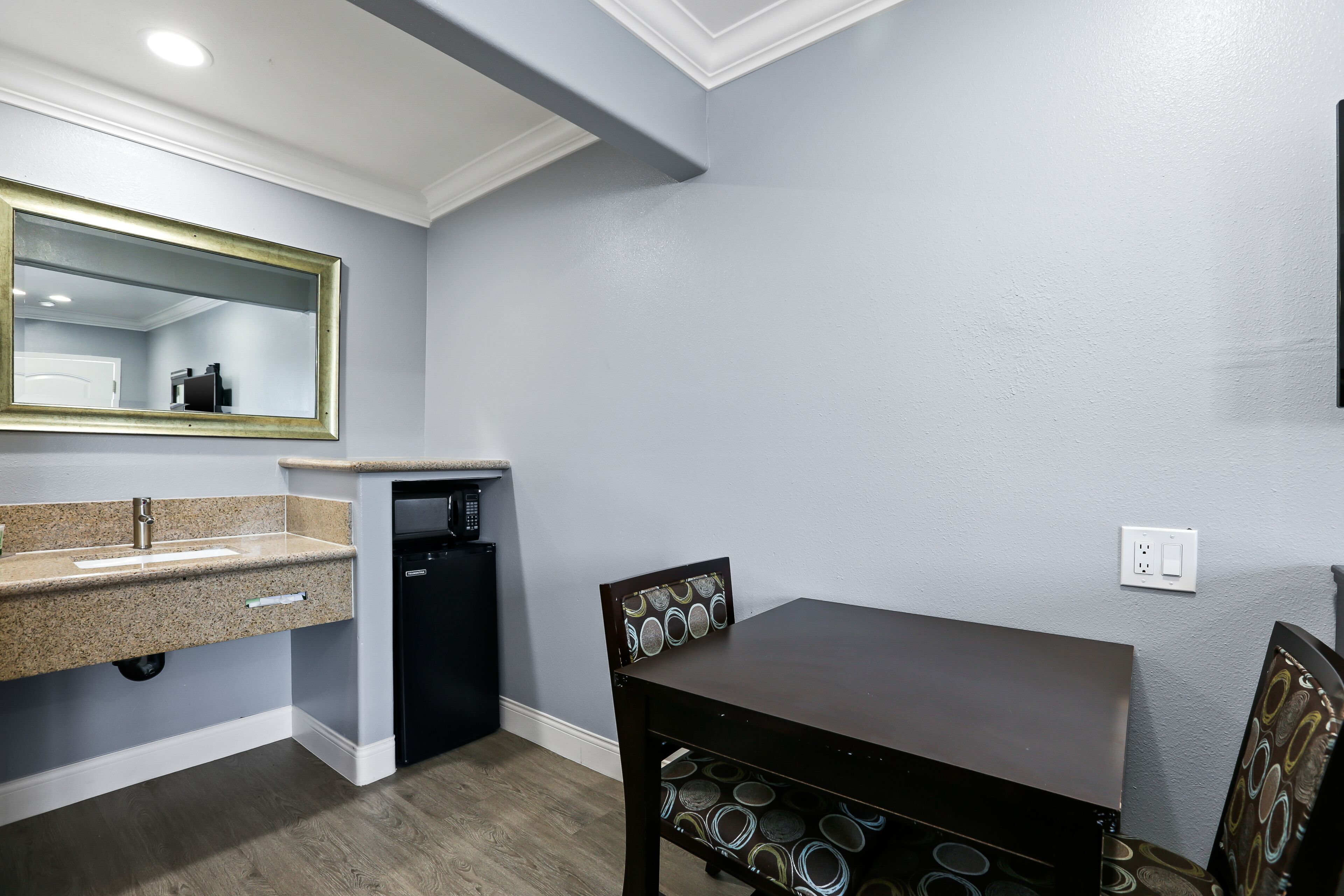 A modern bathroom with a granite countertop sink, a black dishwasher, and a dark wooden table with patterned chairs.