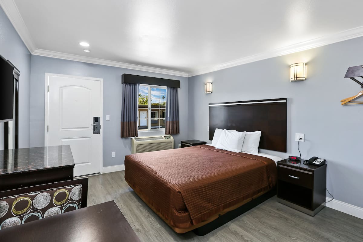 A hotel room with a large bed, bedside tables, a TV, and a window with curtains.