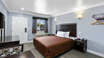A hotel room with a large bed, bedside tables, a TV, and a window with curtains.