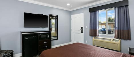Habitación de hotel con cama, escritorio con televisor de pantalla plana, cómoda, espejo, ventana con cortinas y aire acondicionado instalado en la pared.