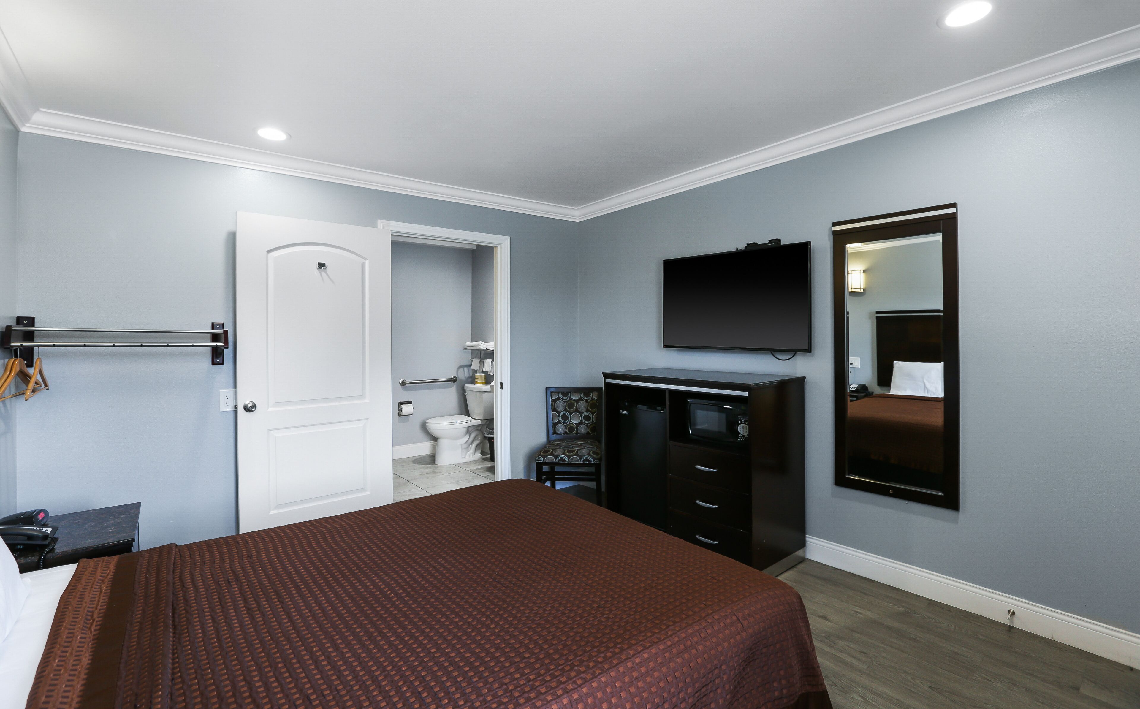 A hotel room with a bed, a dresser, a television, and a bathroom visible through an open door.