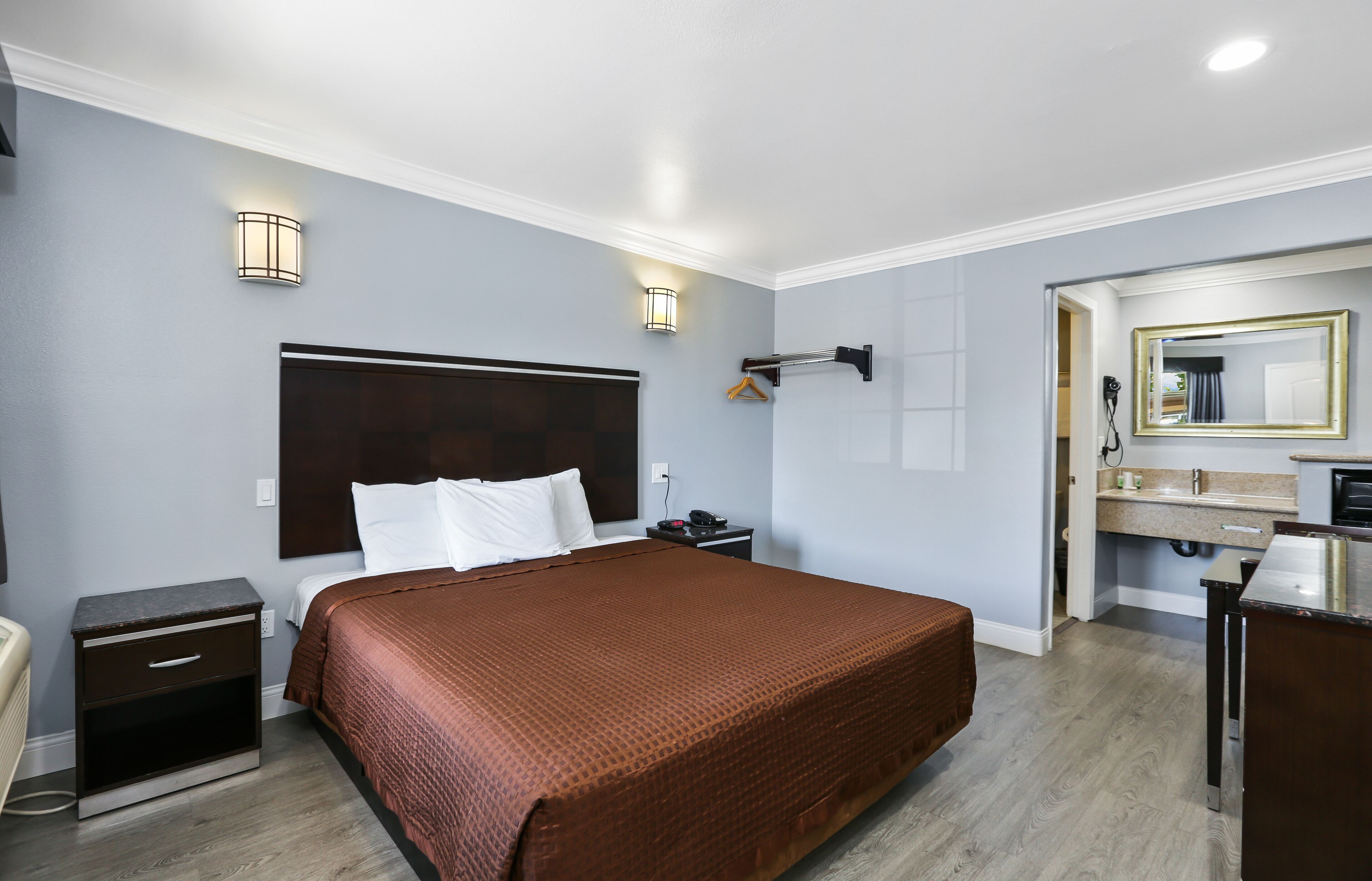 Habitación de hotel con una cama grande, mesitas de noche, cómoda, espejo y baño con lavabo y espejo.