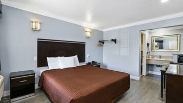 Habitación de hotel con una cama grande, mesitas de noche, cómoda, espejo y baño con lavabo y espejo.
