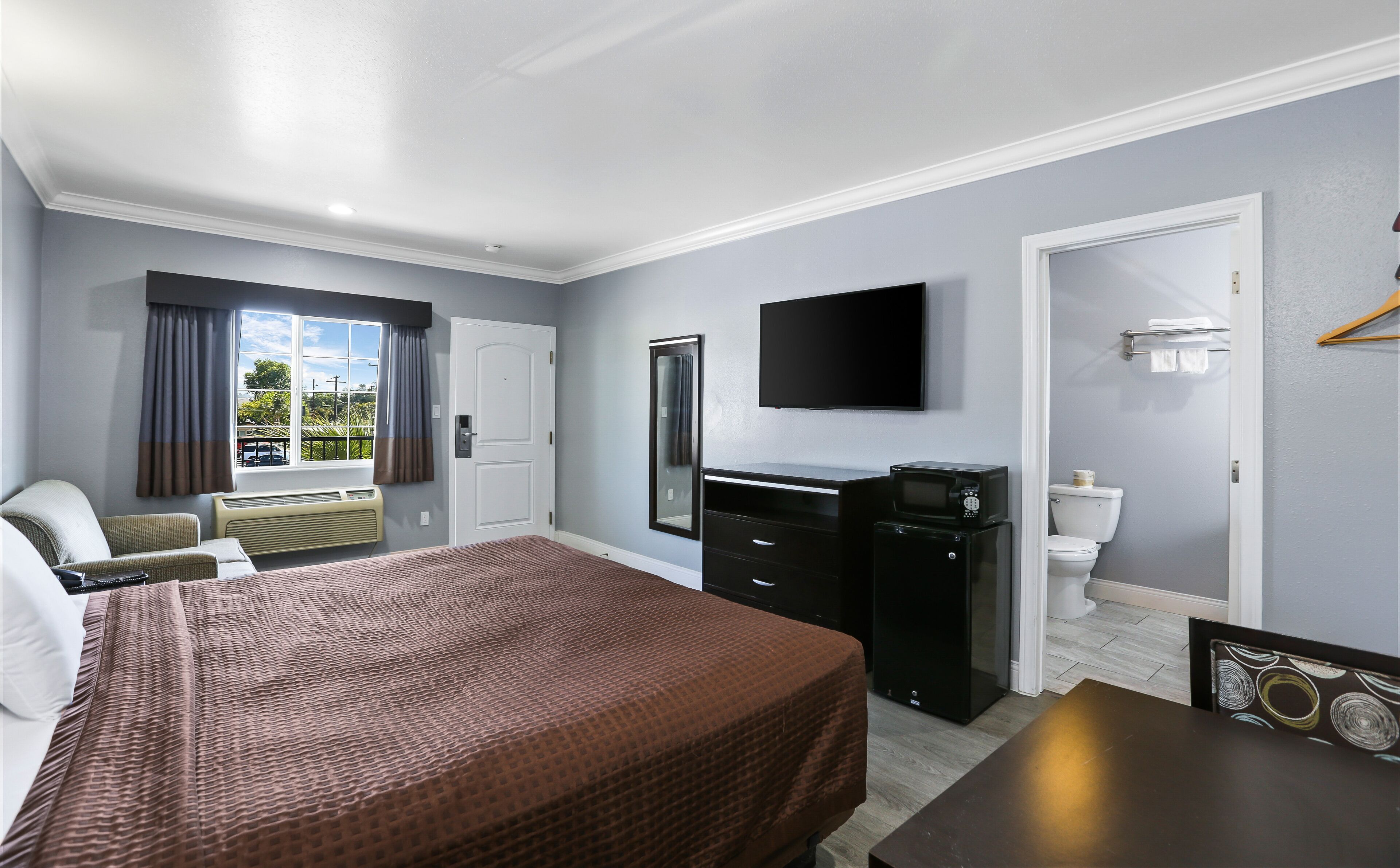 A hotel room with a bed, a desk, a television, a mirror, and a window with curtains.