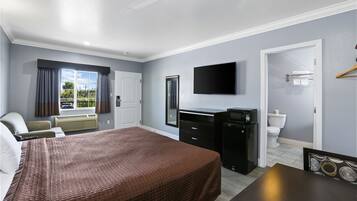 A hotel room with a bed, a desk, a television, a mirror, and a window with curtains.