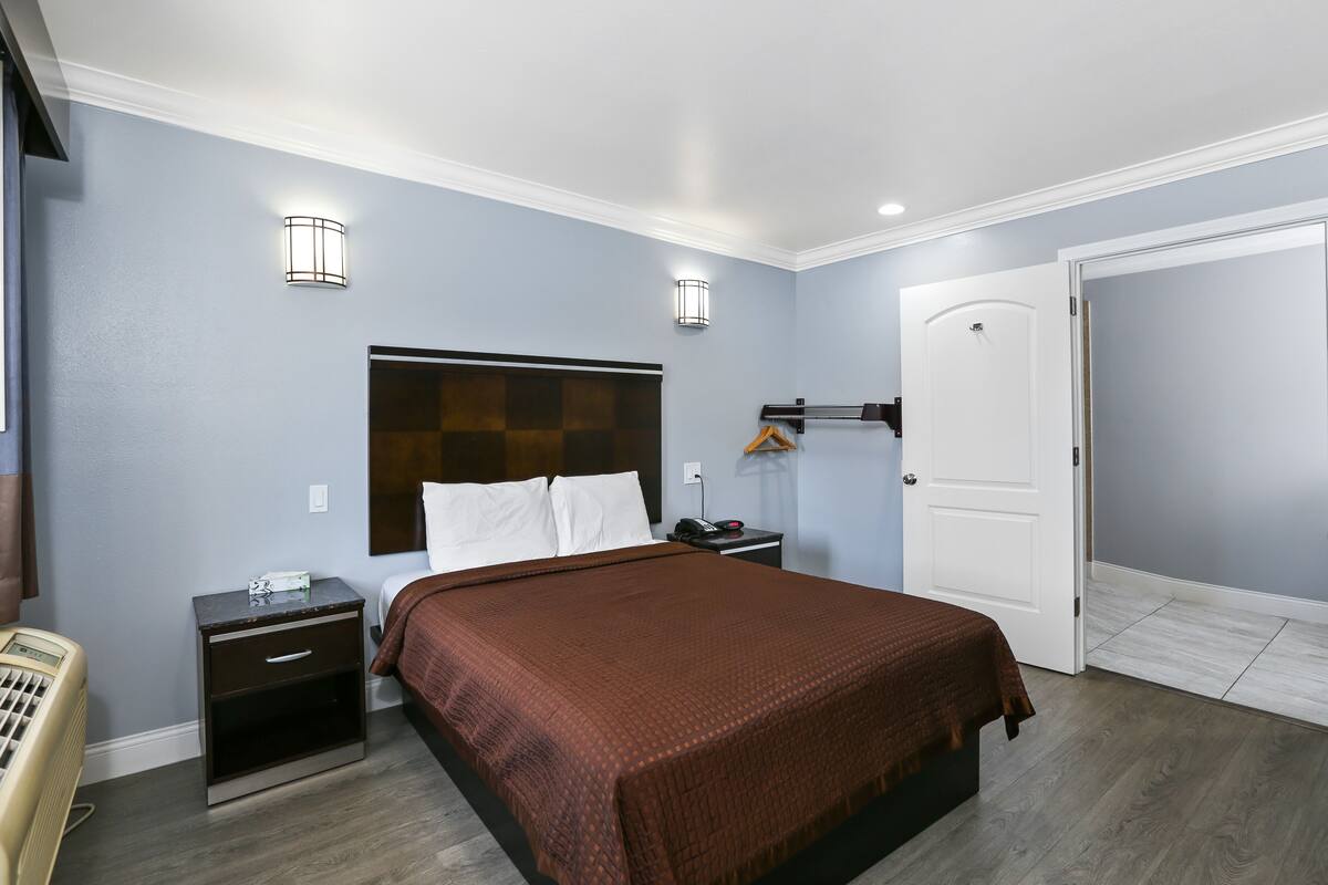 A hotel room with a bed, bedside table, lamp, and a door.