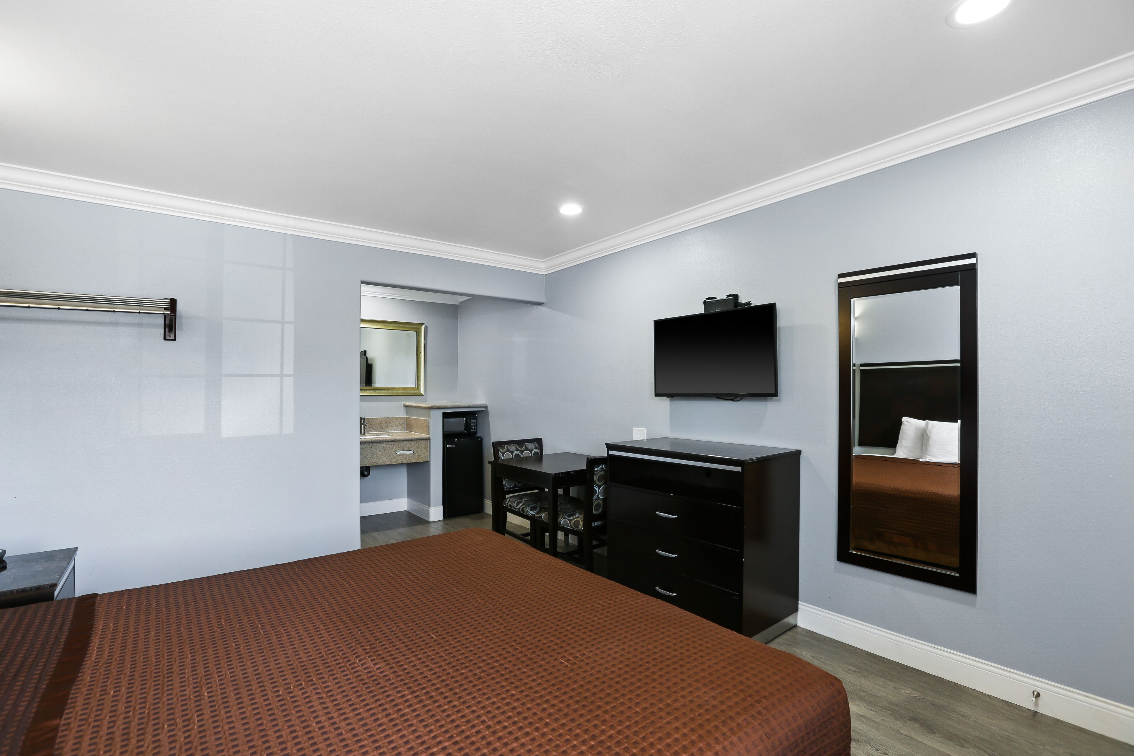 A hotel room with a bed, a desk, a chair, a dresser, a TV, and a mirror.