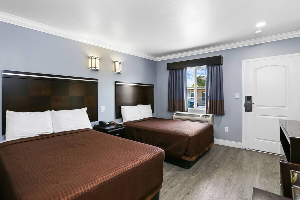 A hotel room with two beds, a desk, a chair, a window with curtains, and a door.