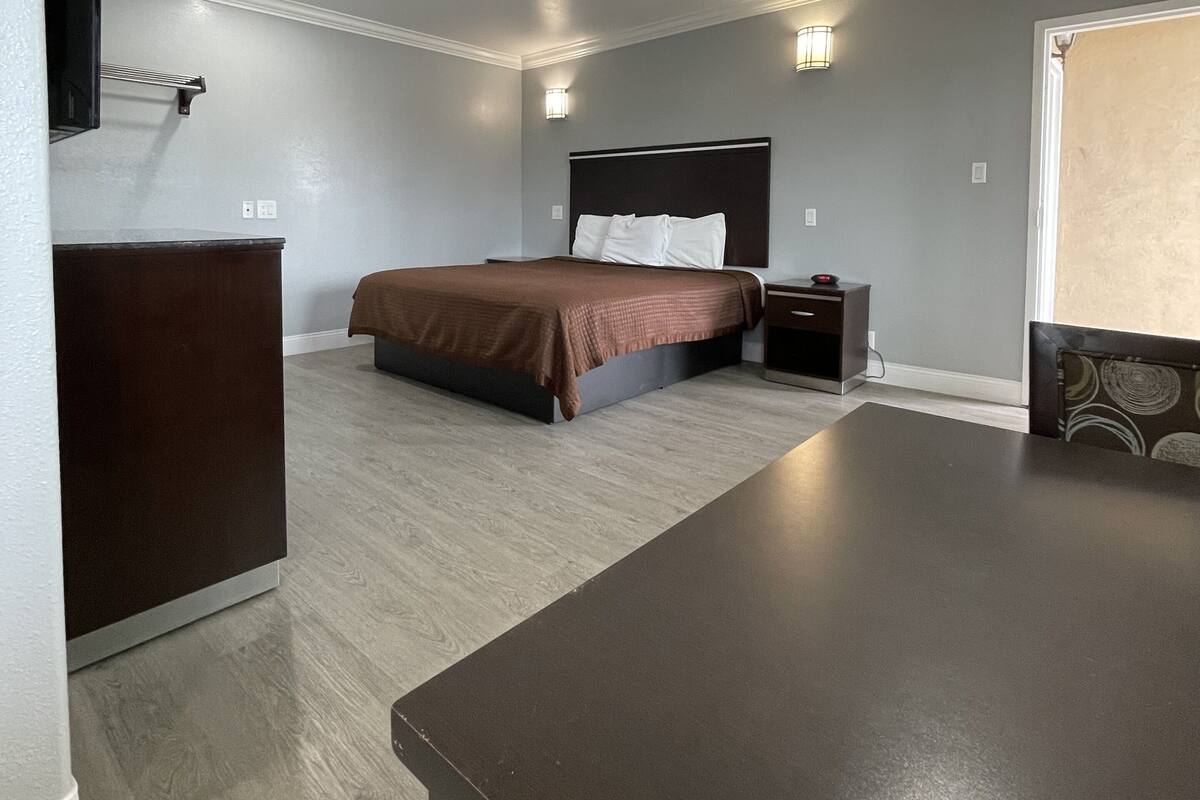 A hotel room with a bed, bedside table, dresser, and a large table.