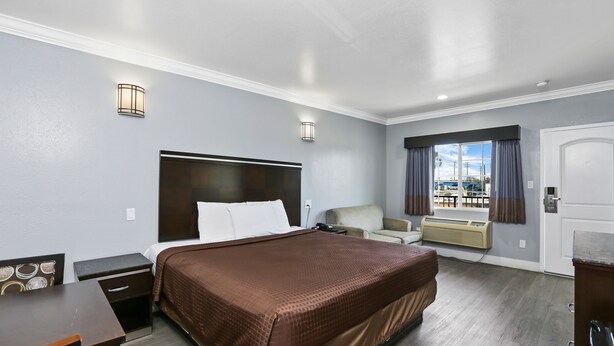 Ein Hotelzimmer mit einem großen Bett, einem Schreibtisch, einem Stuhl, einem Fenster mit Vorhängen und Blick auf den Jachthafen.