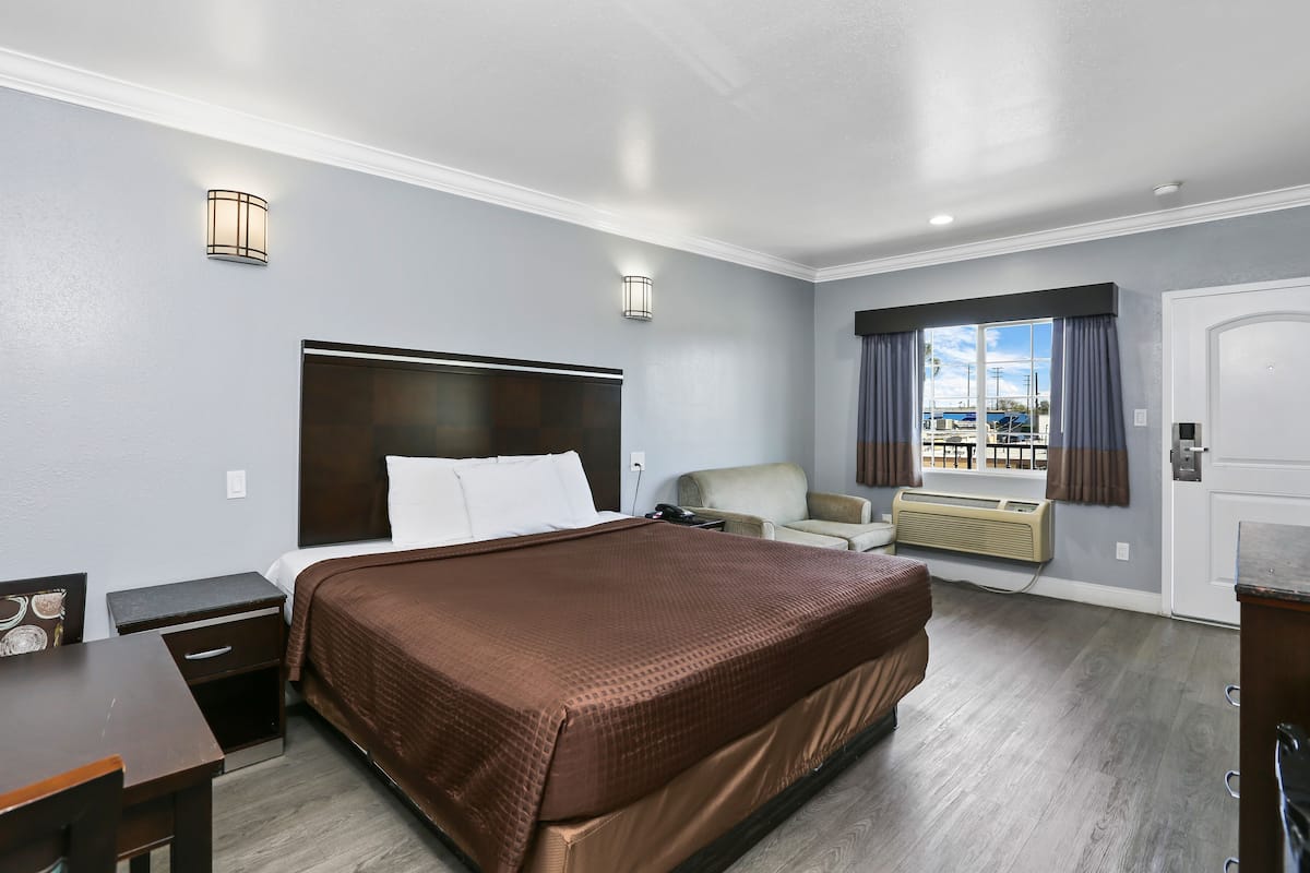 A hotel room with a large bed, a desk, a chair, a window with curtains, and a view of the marina.
