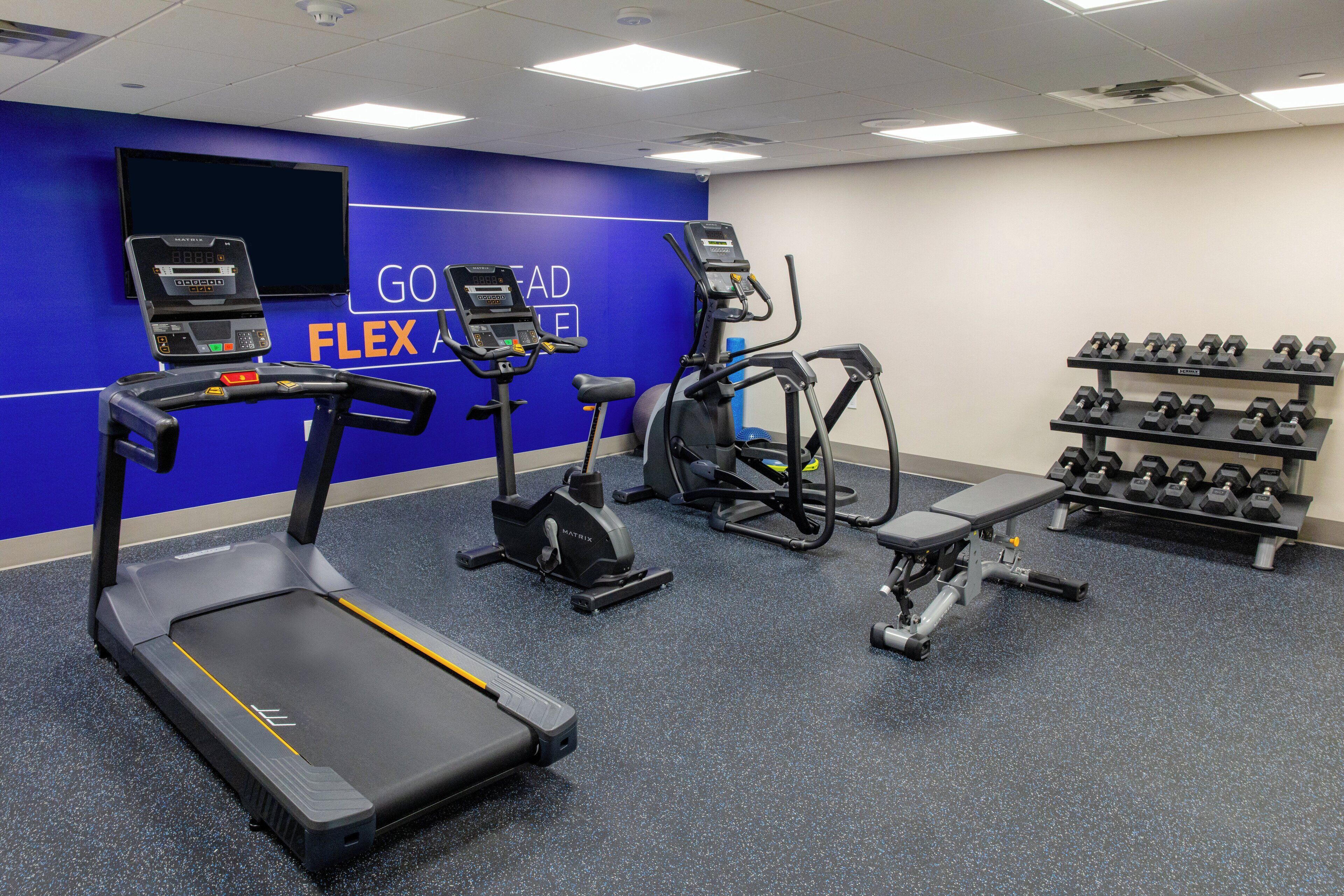 Une salle de sport équipée de tapis de course, de vélos elliptiques et d’un banc de musculation.
