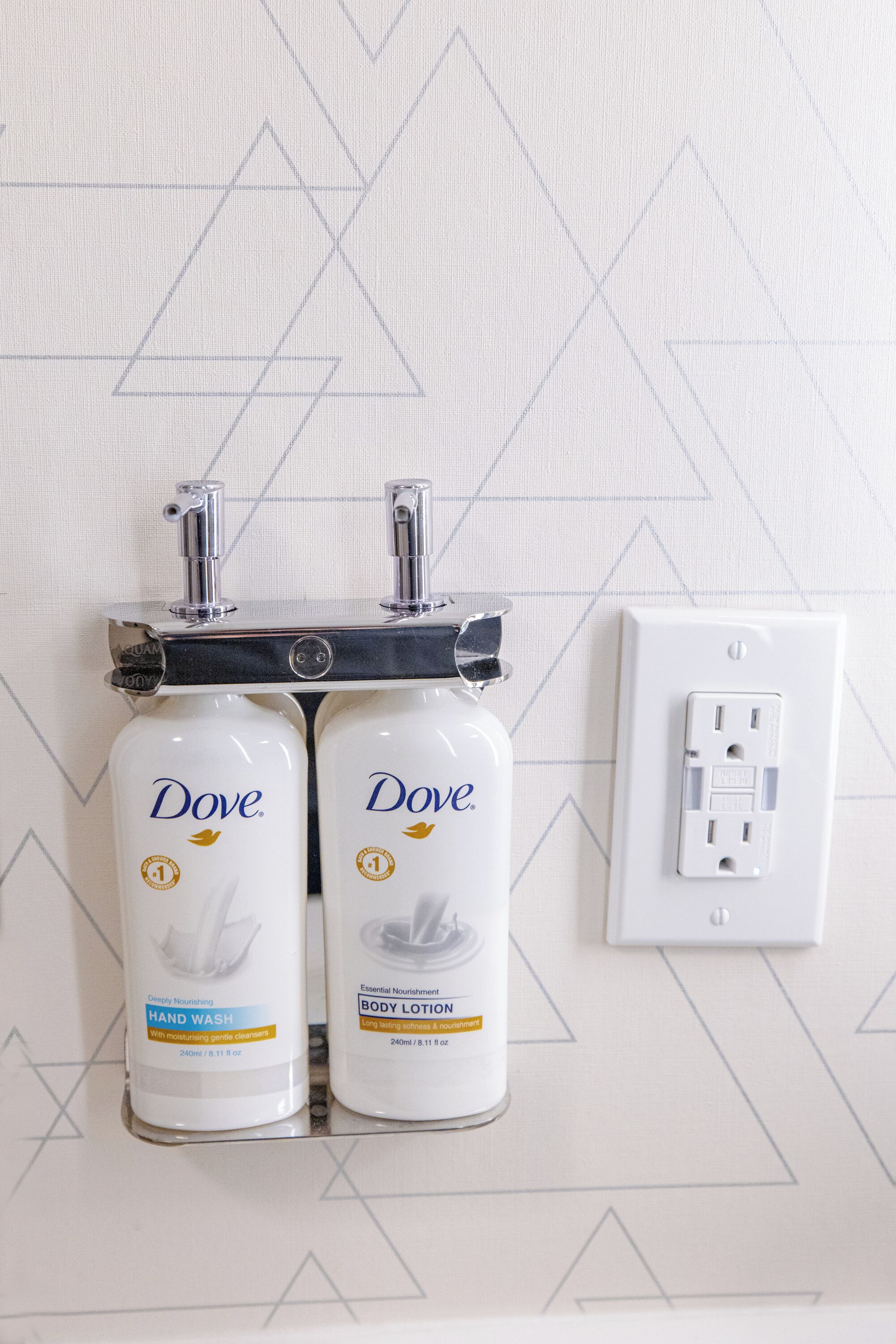 Deux flacons de savon liquide Dove fixés sur un mur orné d’un motif géométrique.