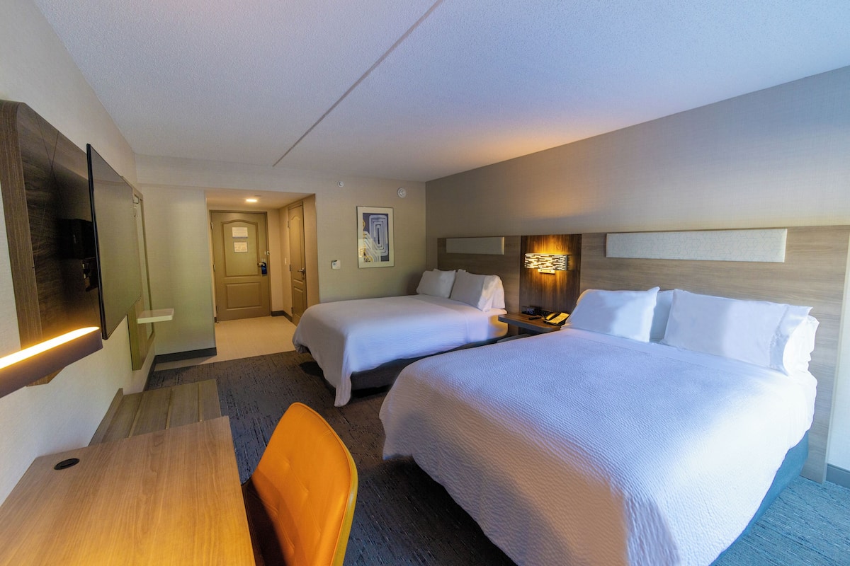 A hotel room with two beds, a desk, a chair, a TV, and a nightstand.