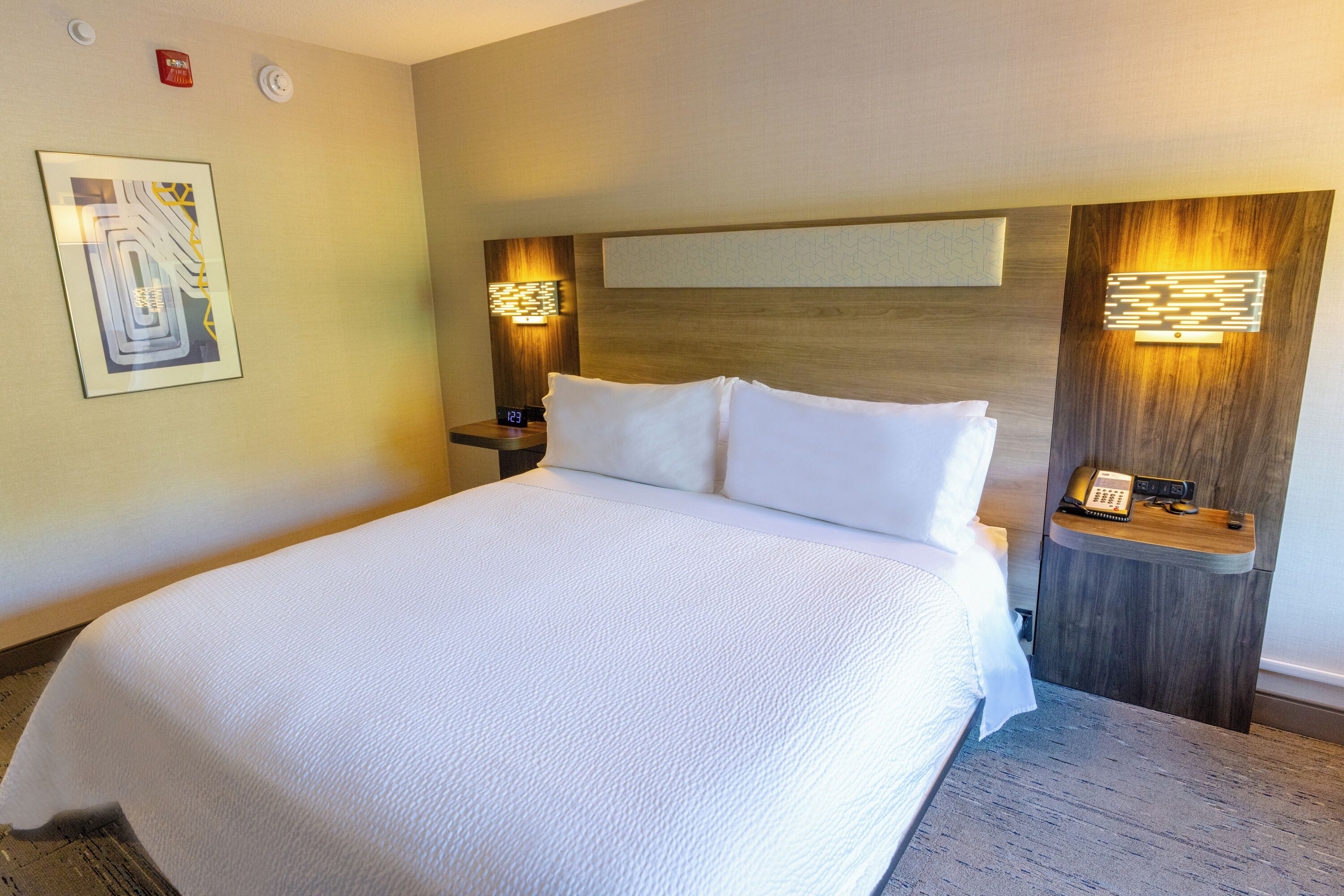 A hotel room with a large bed, a nightstand with a phone, and wall-mounted lighting.