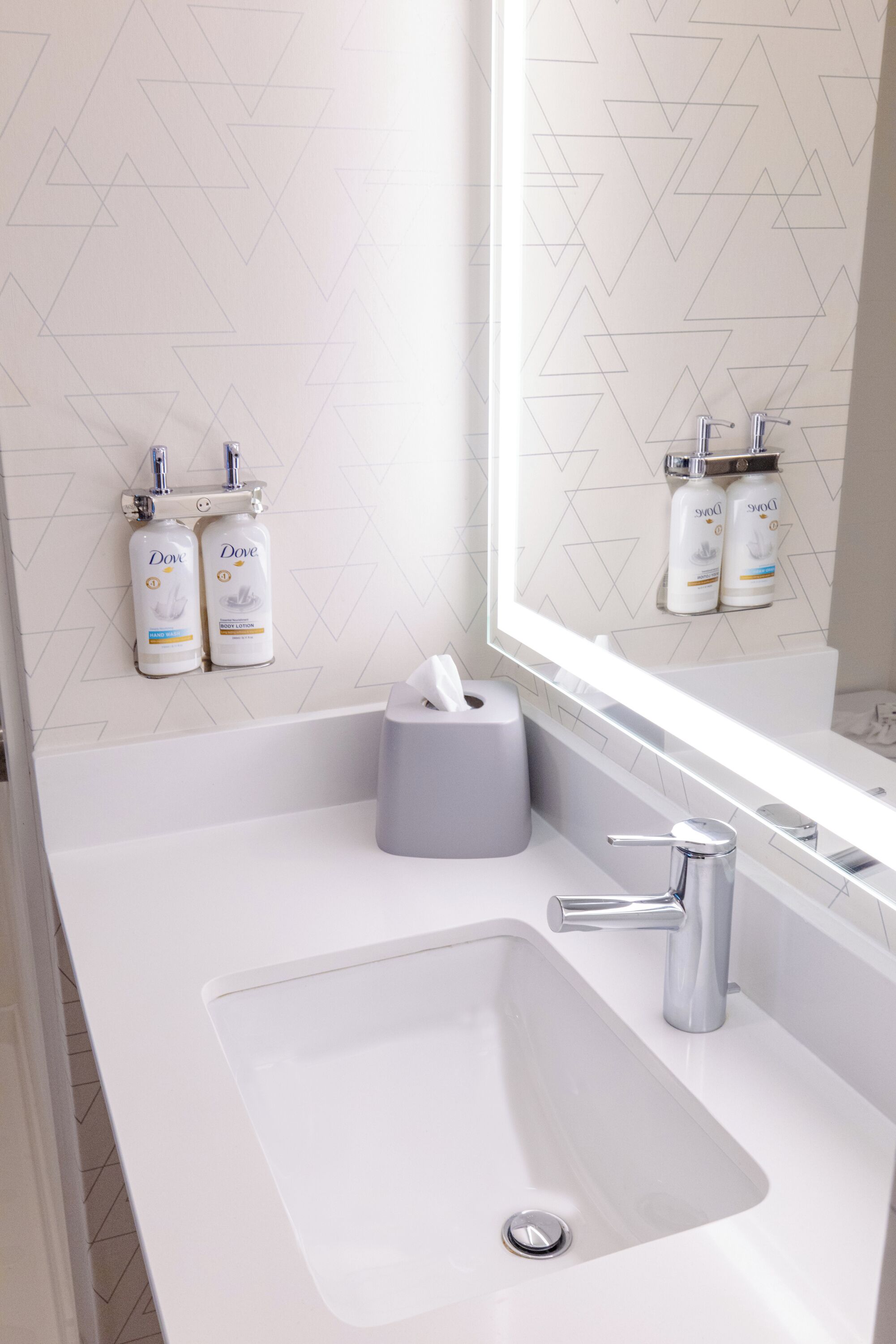 Un baño con un lavabo blanco, un espejo y dispensadores de jabón Dove en la pared.