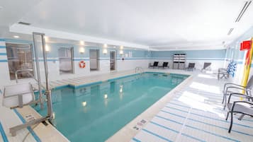 A swimming pool with clear blue water, tiled floor, and lounge chairs.