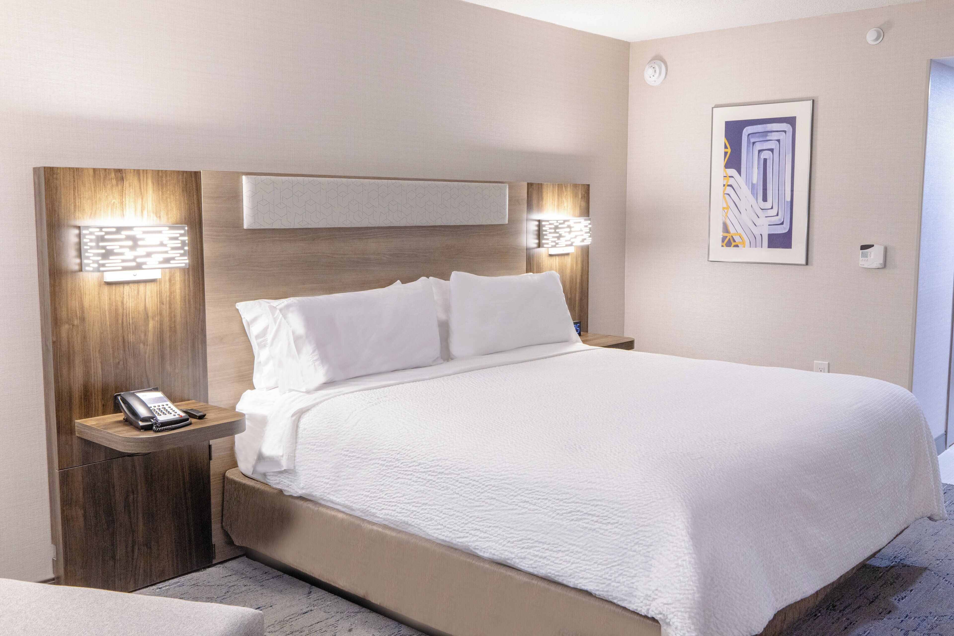Una habitación de hotel moderna con una cama grande, teléfono en la mesita de noche e iluminación en la pared.