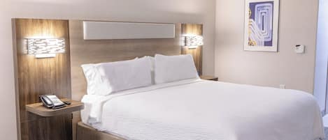 Una habitación de hotel moderna con una cama grande, teléfono en la mesita de noche e iluminación en la pared.