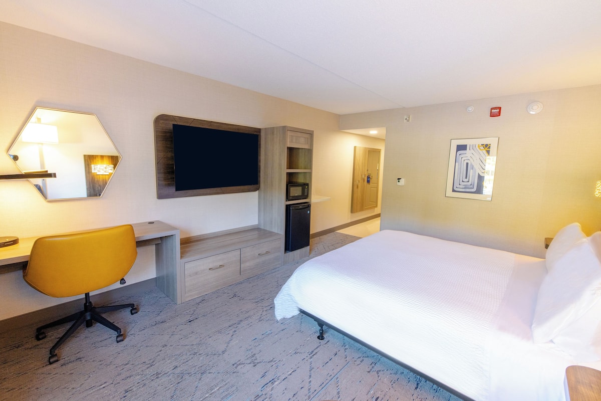 A hotel room with a bed, a desk with a chair, a microwave, and a small cabinet.
