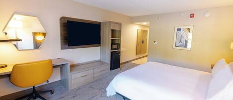 A hotel room with a bed, a desk with a chair, a microwave, and a small cabinet.