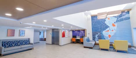 Een ruime lobby met een modern design, met een zithoek met banken en stoelen, een receptiebalie en een grote muurkaart.