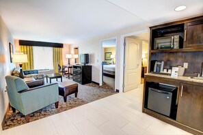 A hotel room with a living area, kitchenette, and a separate bedroom.