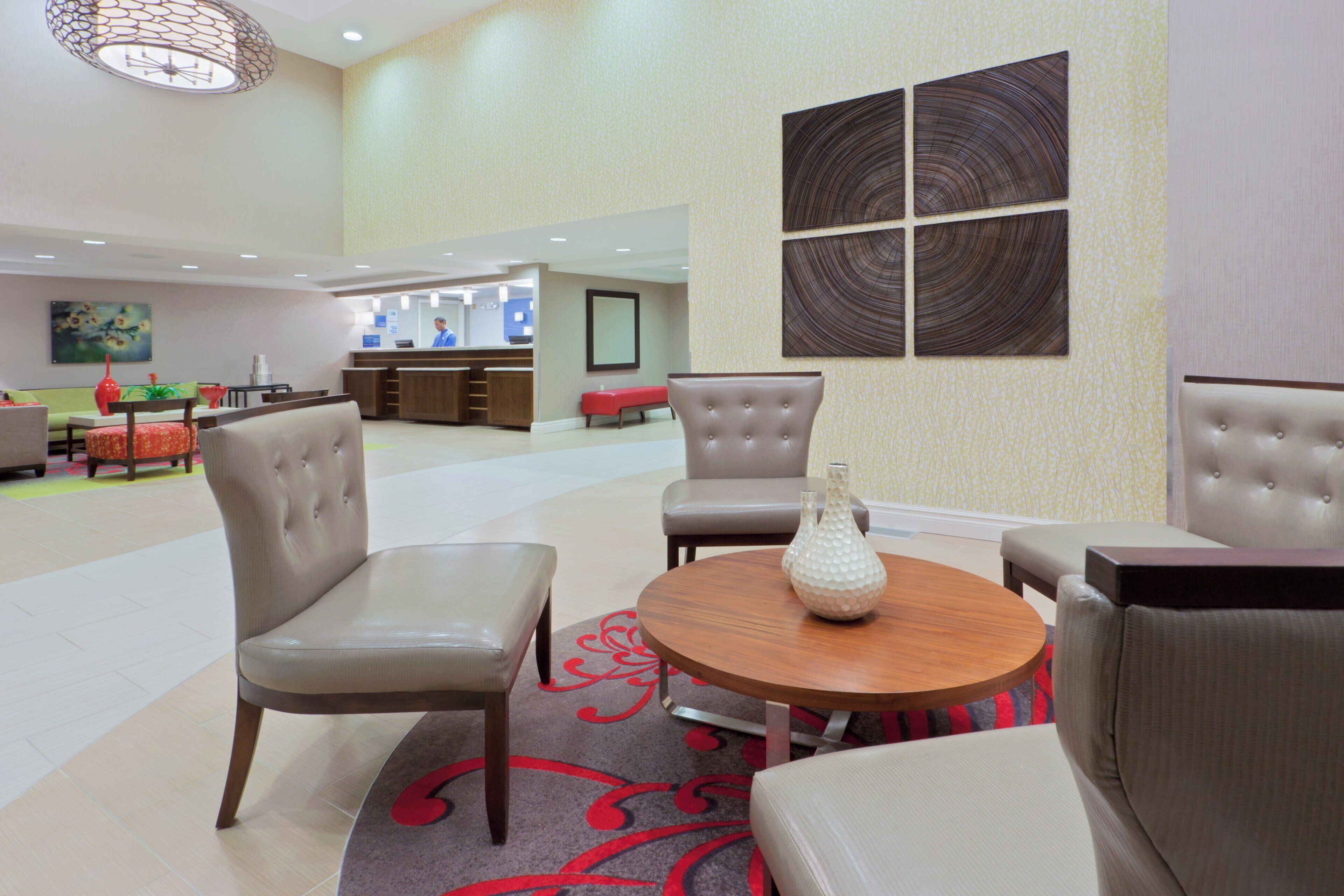 A hotel lobby with a reception desk, seating area with chairs and a table, and a large abstract wall art piece.
