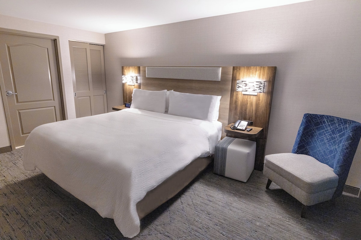 A hotel room with a large bed, a nightstand with a phone, a chair, and a door.