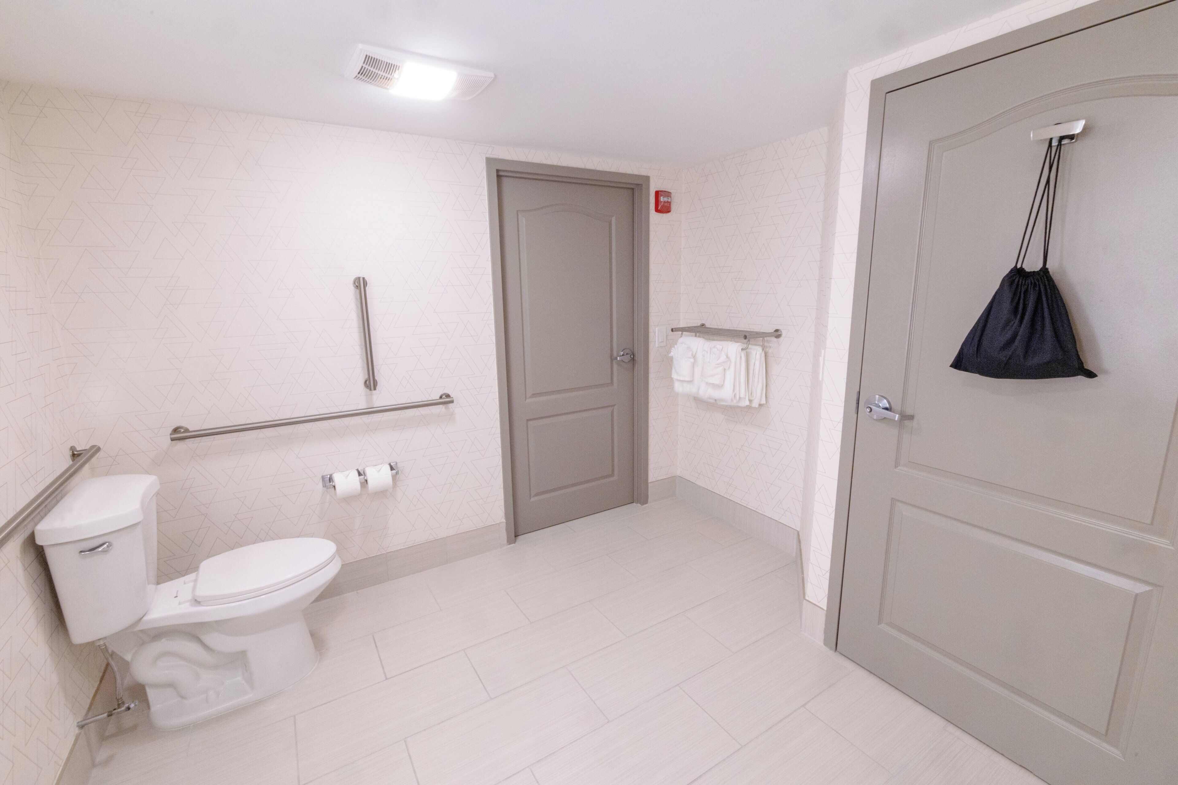 A bathroom with a toilet, handrail, towel rack, and a door.