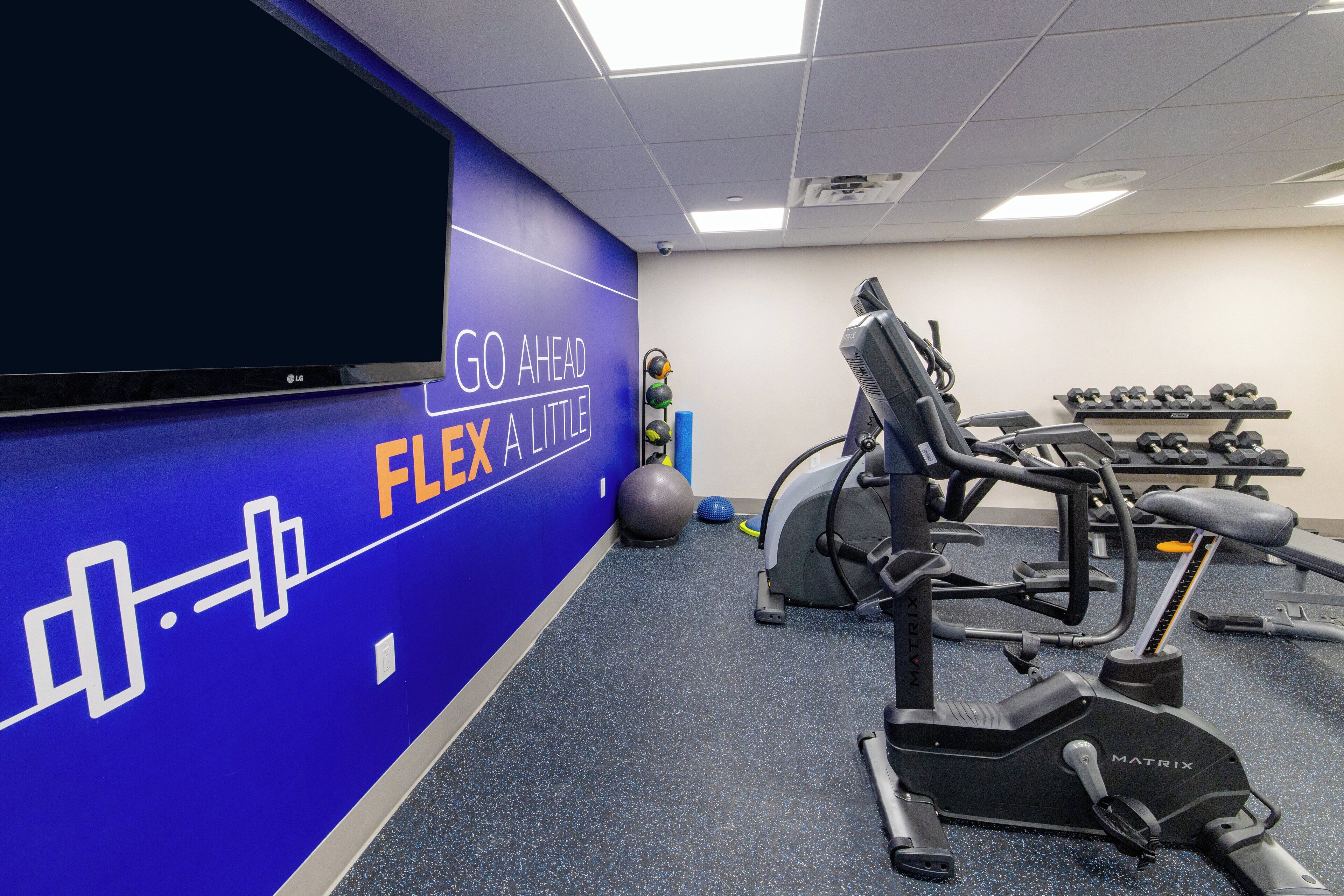 A gym with exercise equipment, a blue wall with motivational text, and a large screen.