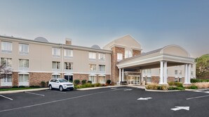 A multi-story hotel with a covered entrance, parking lot, and a white SUV parked in the lot.