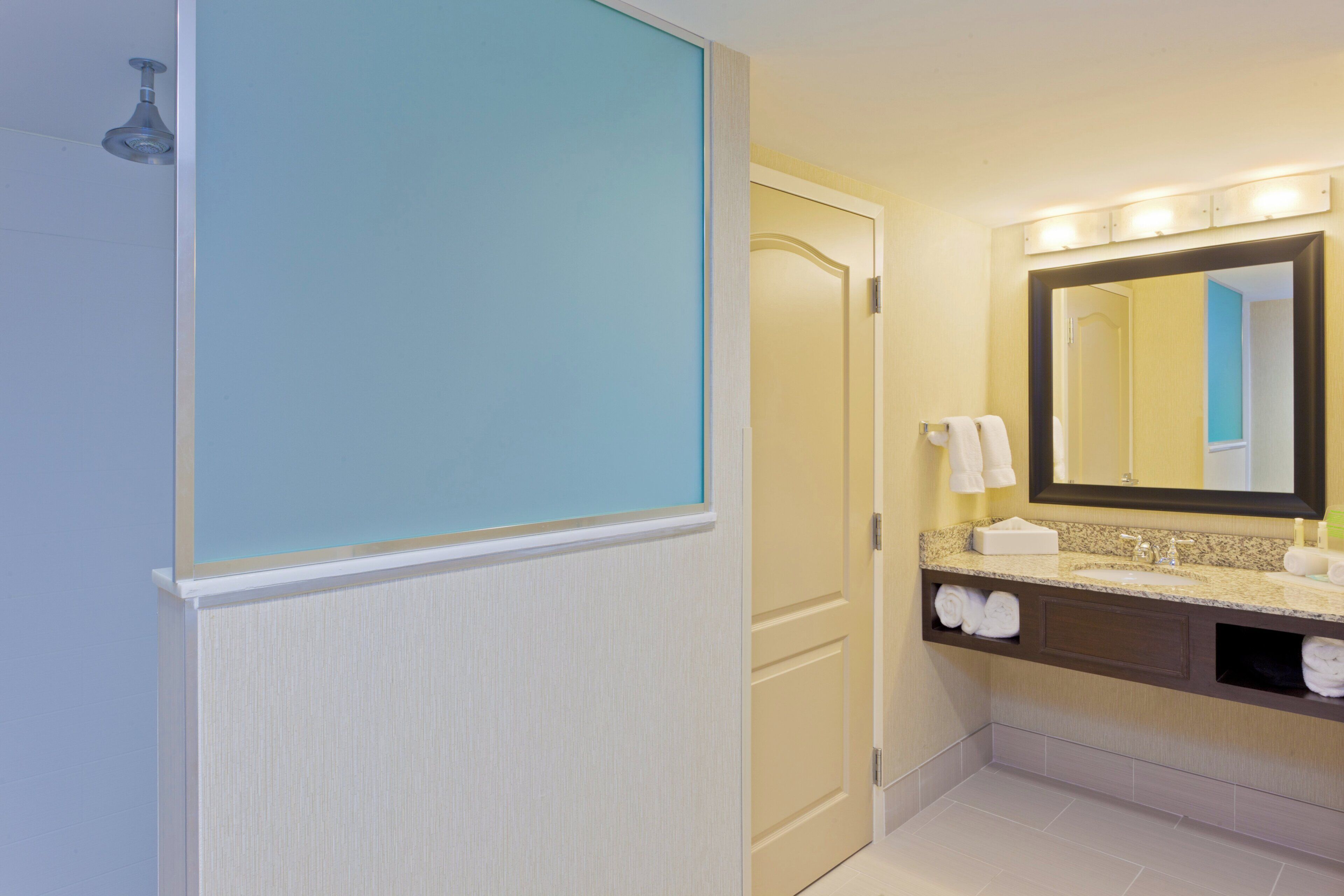 A hotel bathroom with a shower, a sink, a mirror, and towels.