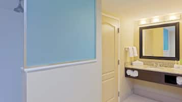 A hotel bathroom with a shower, a sink, a mirror, and towels.