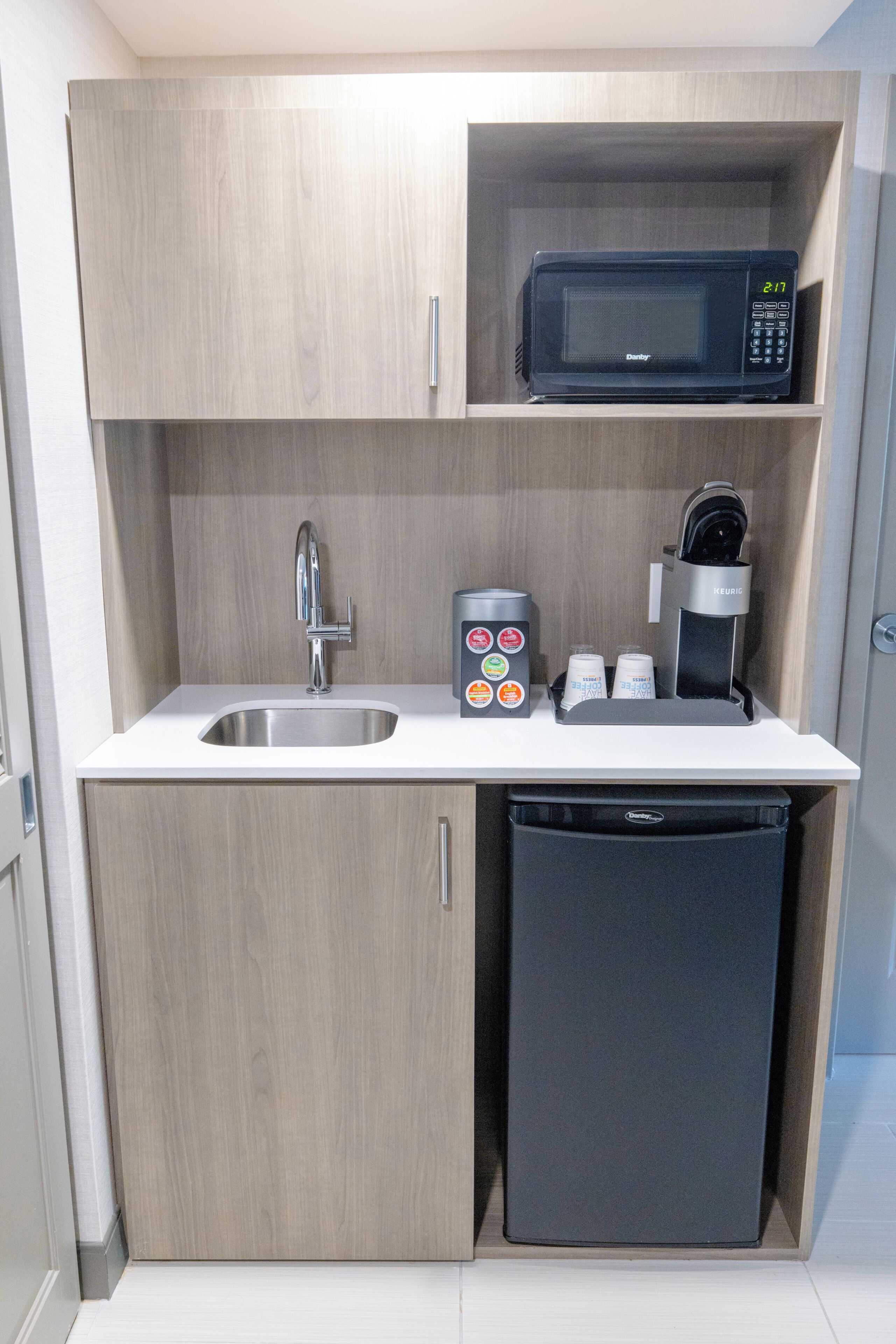 Una kitchenette compacta con microondas, cafetera y lavamanos.