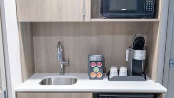 Una kitchenette compacta con microondas, cafetera y lavamanos.