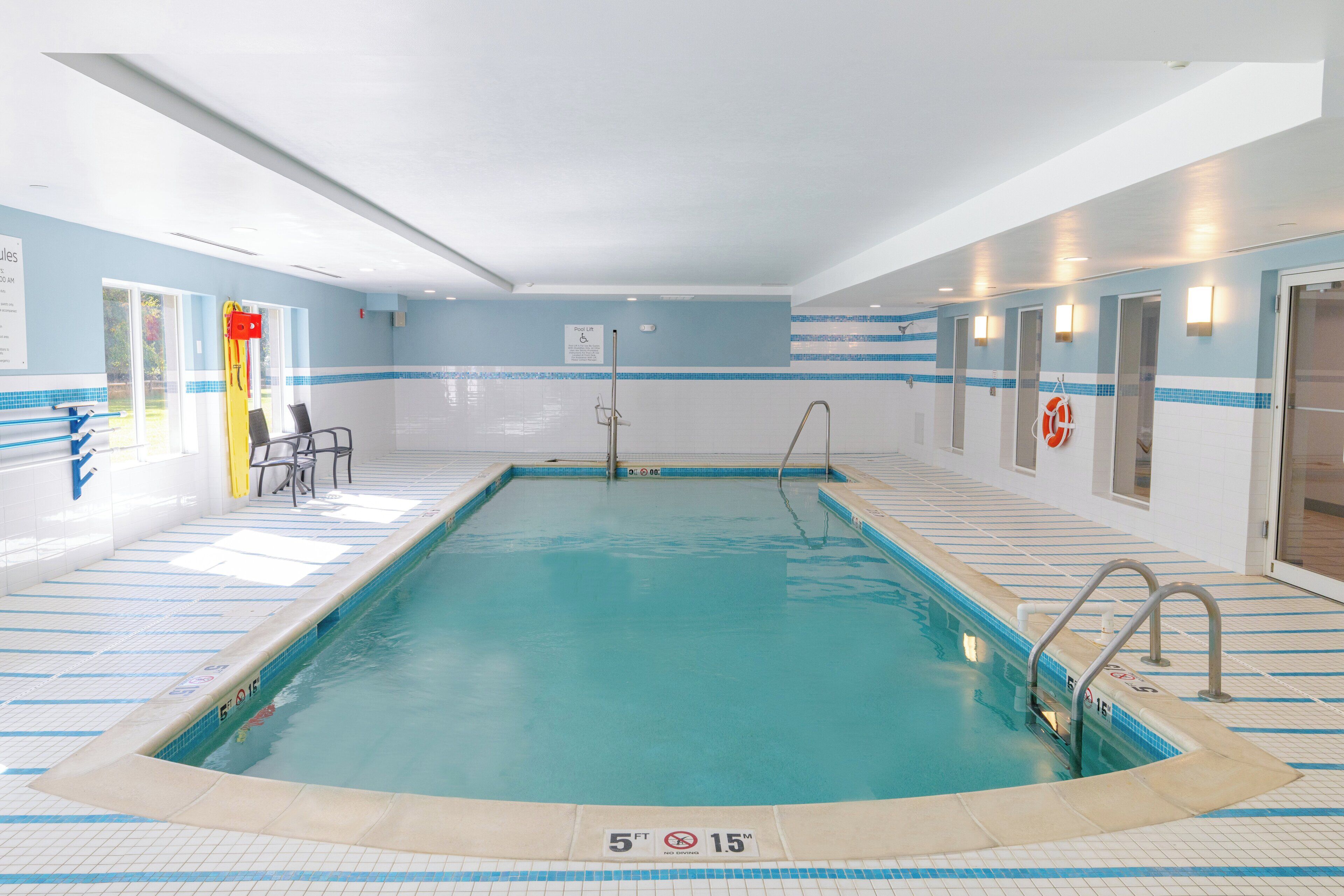 An indoor swimming pool with clear lane markings, a lifeguard chair, and a sign indicating the pool depth.