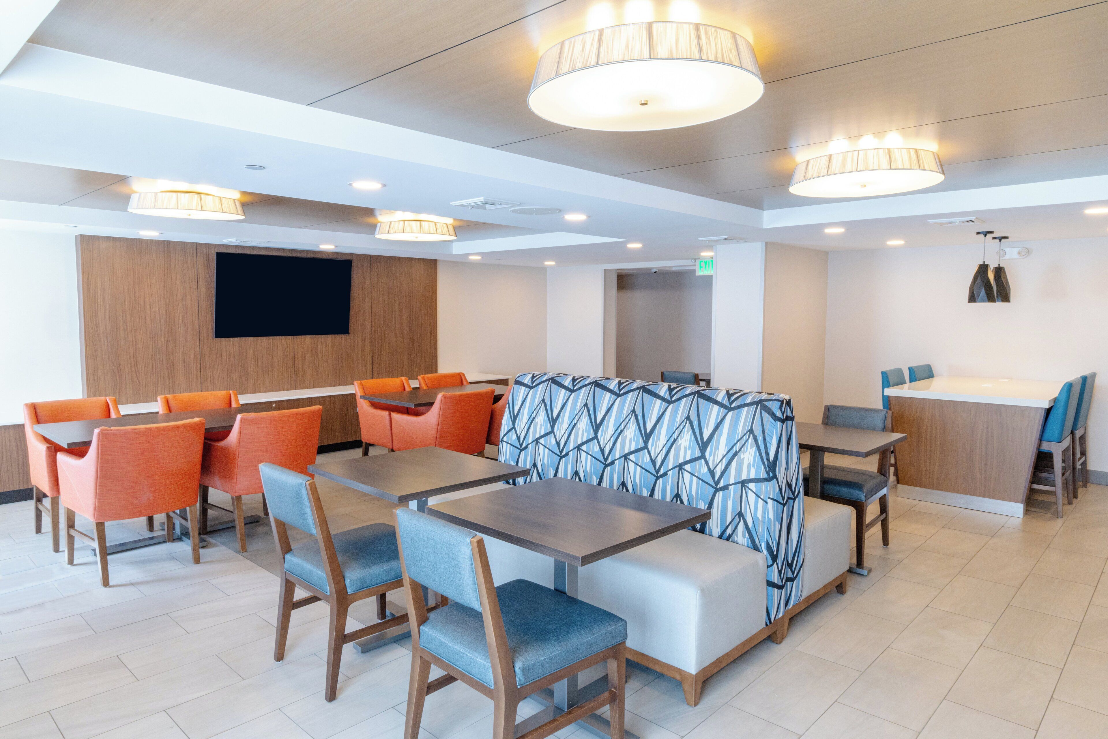A modern dining area with tables and chairs, a central seating area, and a flat-screen TV mounted on the wall.