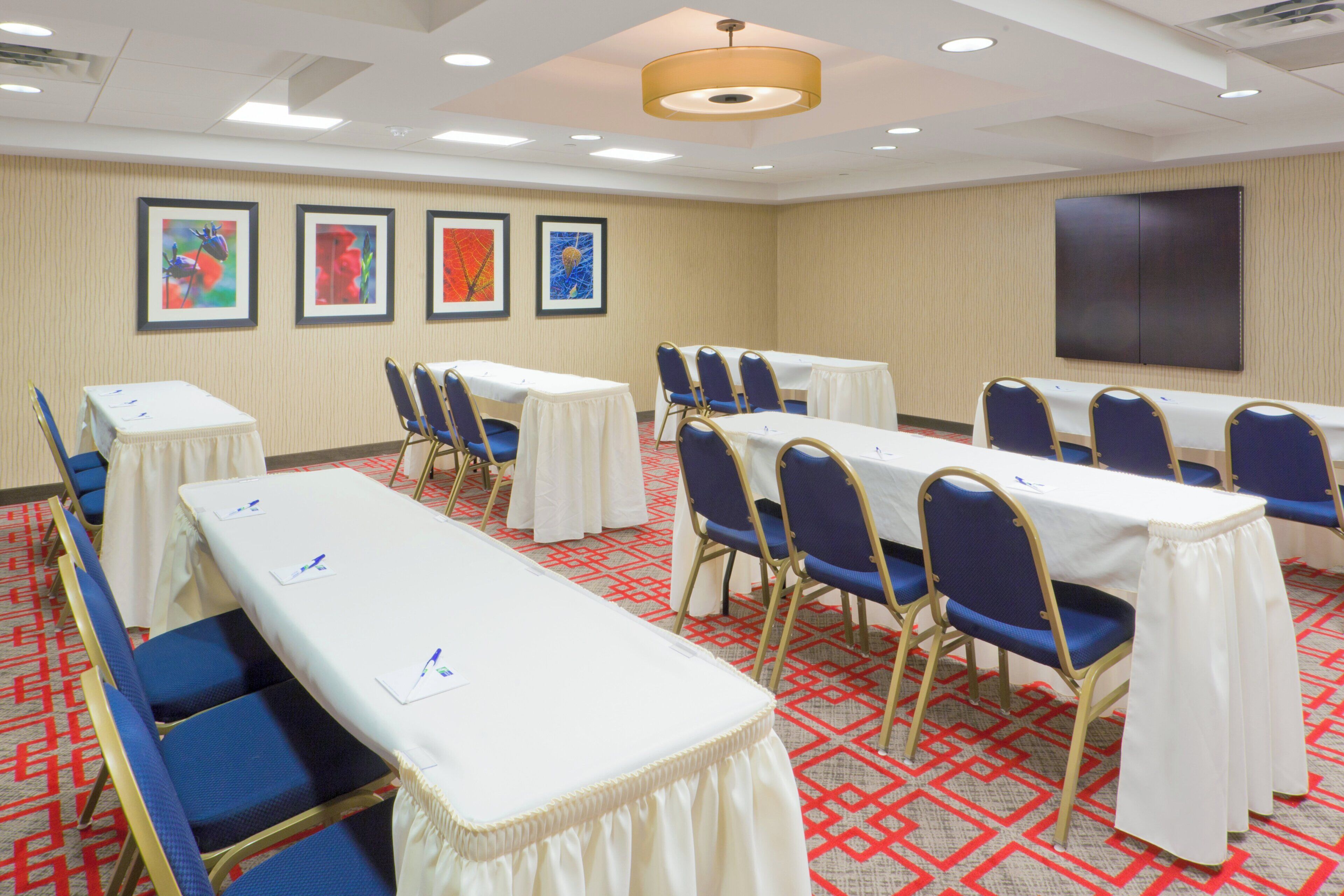 A conference room with tables and chairs, framed artwork on the walls, and a carpeted floor.